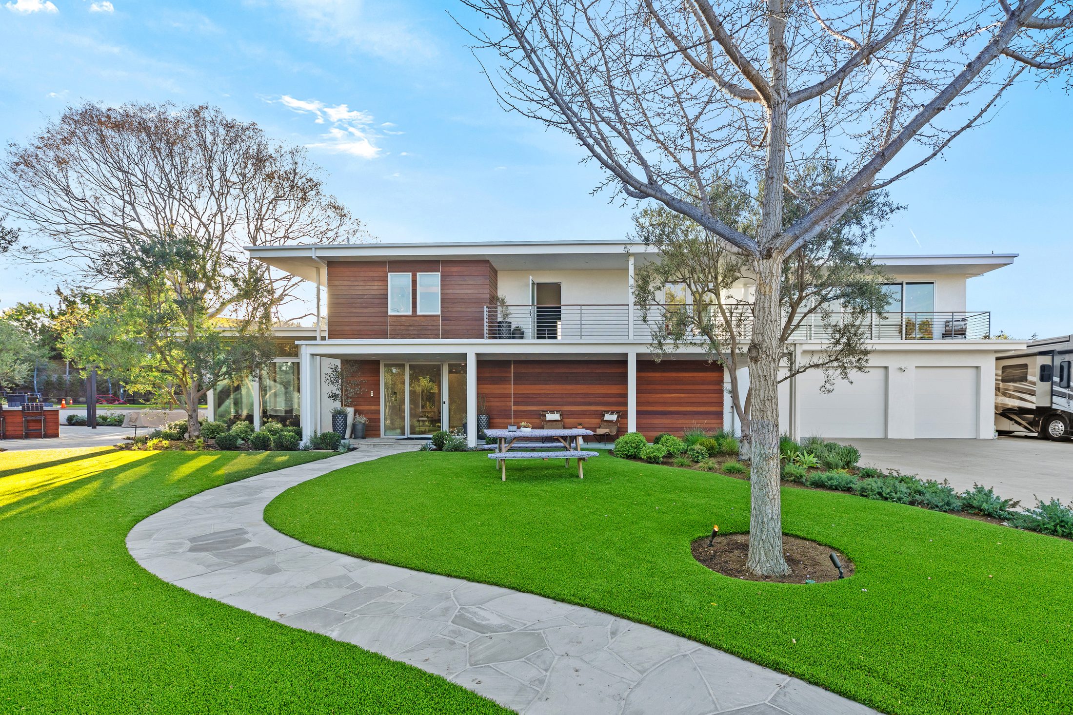 Modern custom home exterior with curving stone path, mature tree, and wood-clad facade — Shipwright Homes new construction
